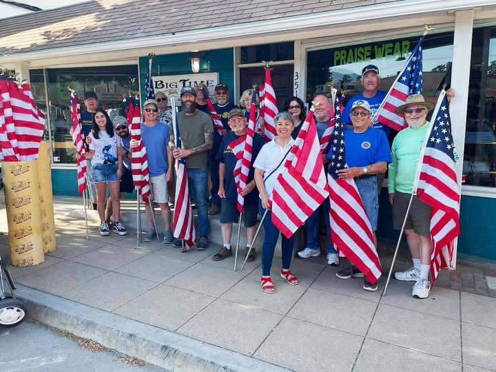 Yucaipa Rotary members in front of a storefront holding United States flags