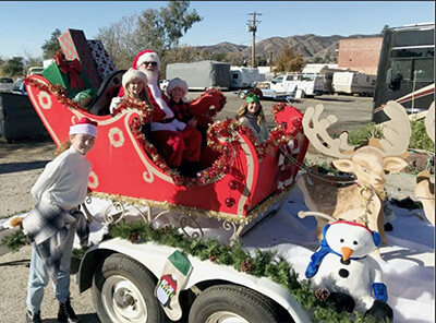 Santa Claus and children ride in a decorated sleigh float with wrapped gifts, a reindeer, and a snowman during the Yucaipa Christmas Parade