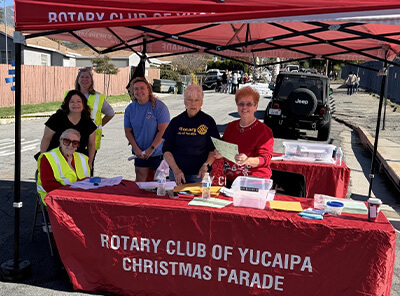 Rotary Club of Yucaipa volunteers staff a registration table under a canopy, welcoming participants during the Yucaipa Christmas Parade.